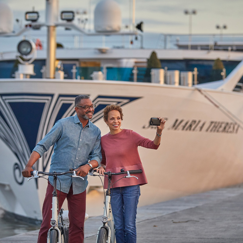 Couple taking a selfie with their bicycles in front of a river cruise ship